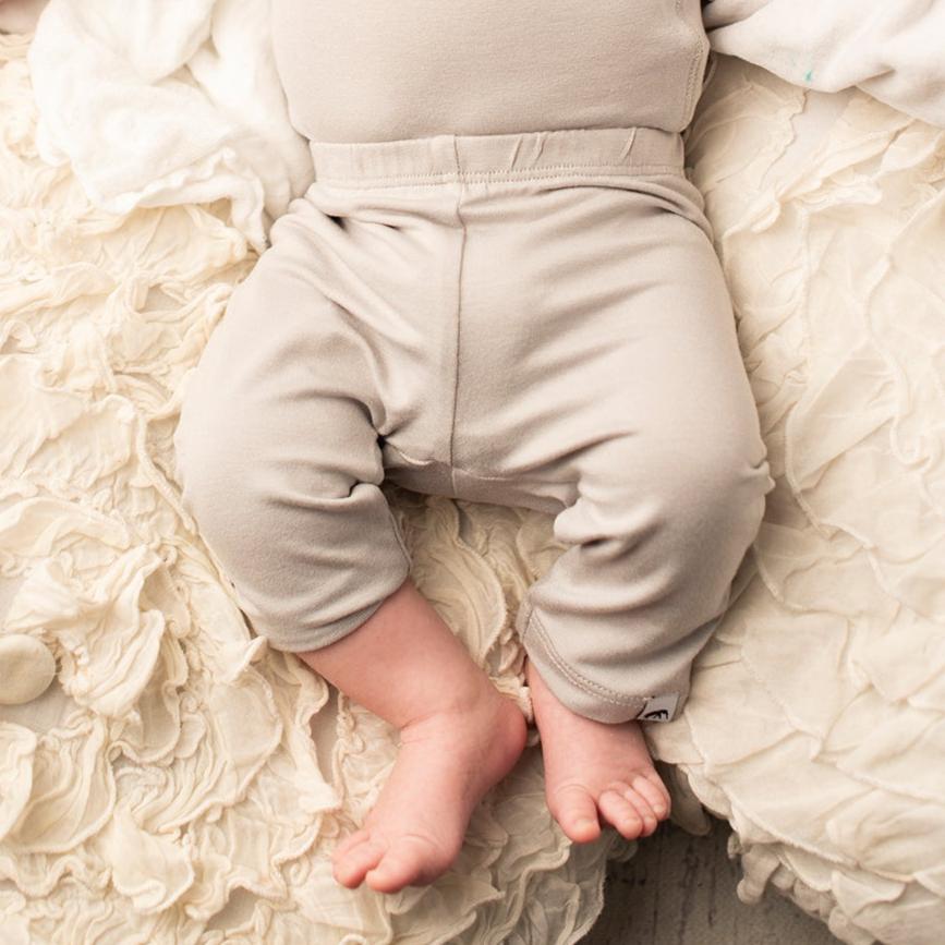 Baby wearing light gray pants on a soft, textured white blanket