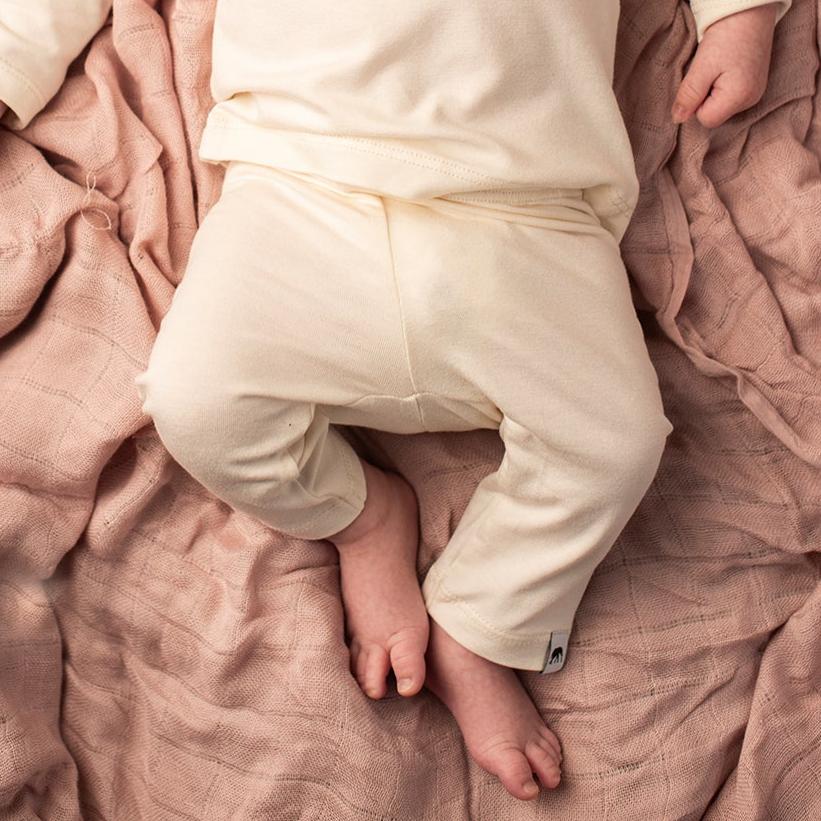 Baby legs in white pants on a soft pink blanket