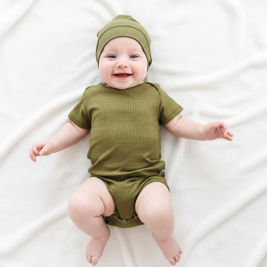 Baby in a green outfit and hat sitting on a green blanket