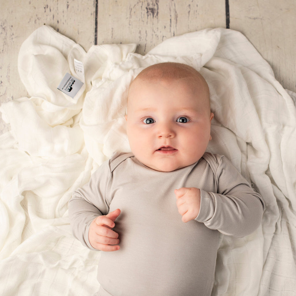Baby in a gray onesie lying on a white blanket